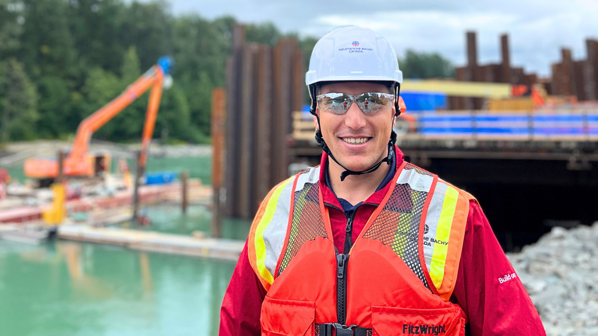Worker facing the camera and smiling, with a marine jobsite in the background
