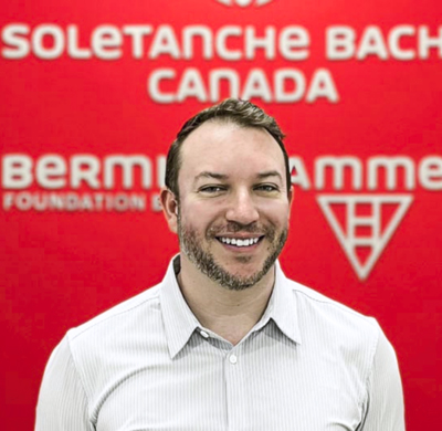 Photo of Mike Mason in SBC's office with a red background and the Soletanche Bachy Canada and Berminghammer logos