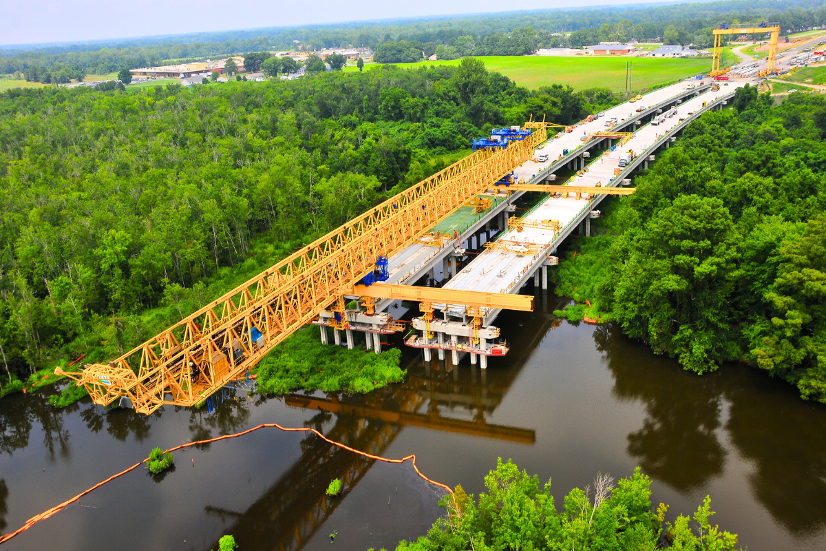 construction site of a road above the water surrounded by green trees