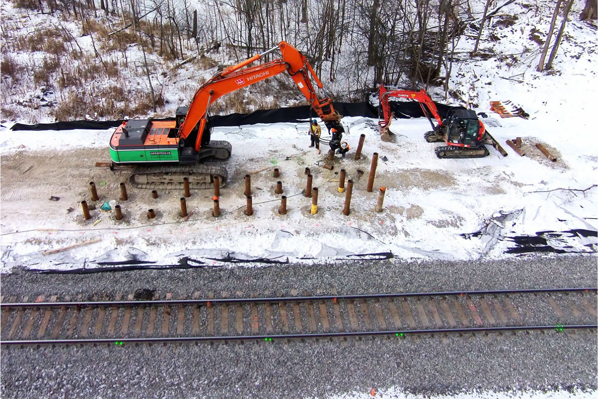 Jobsite with helical pile insertion on frozen ground next to a railway